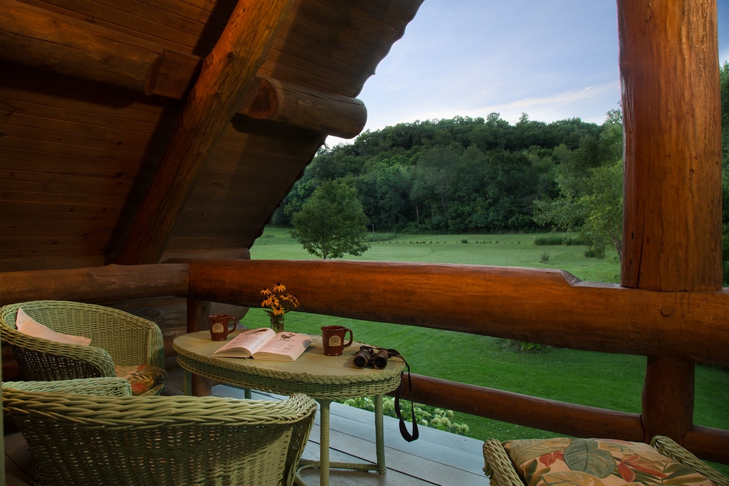 Balcony with green wicker furniture and views of a lush green open lawn and treeline beyond.