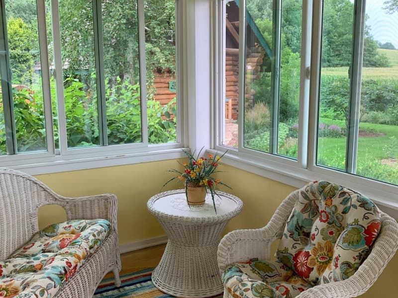 A white wicker furniture set with floral cushions invites you to sit awhile on the porch with windows on three sides.