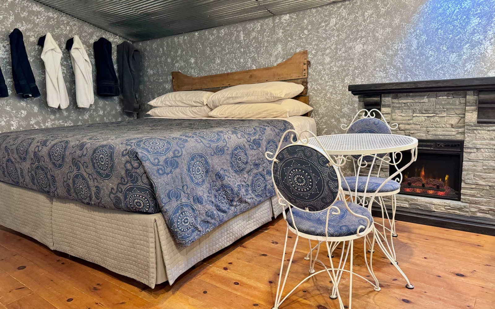 Next to the king bed is a fireplace and in front of the fireplace is a white metal dinette set with a round table and two matching chairs.