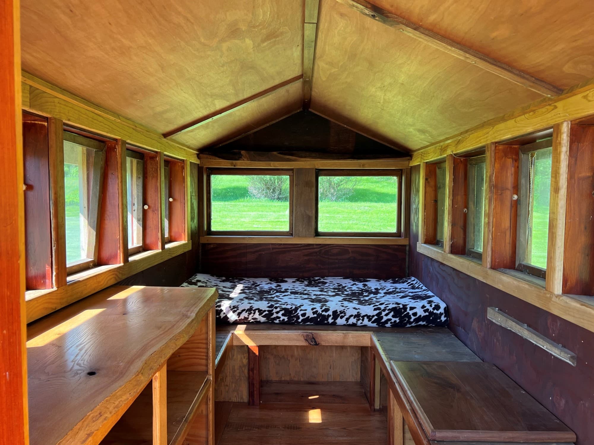 The interior of the Snuggalo is rustic and cozy with wooden shelves lining the low walls, windows all around and a narrow walkway between leading to the bed area at the far end.