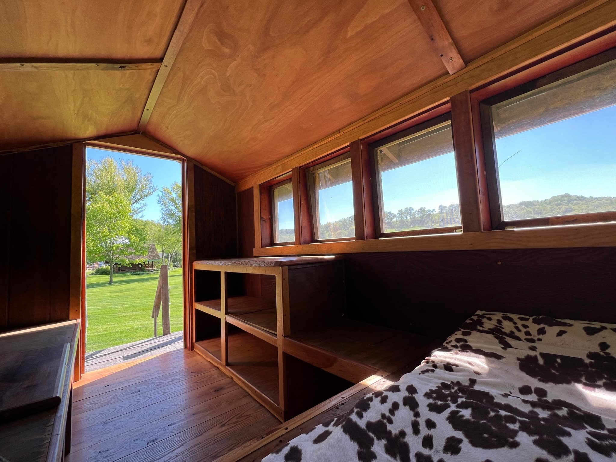 Interior right side of the Snuggalo from the bed area shows wooden shelving along the walls, a bank of windows above the shelving, and the doorway leading to the stairs outside.