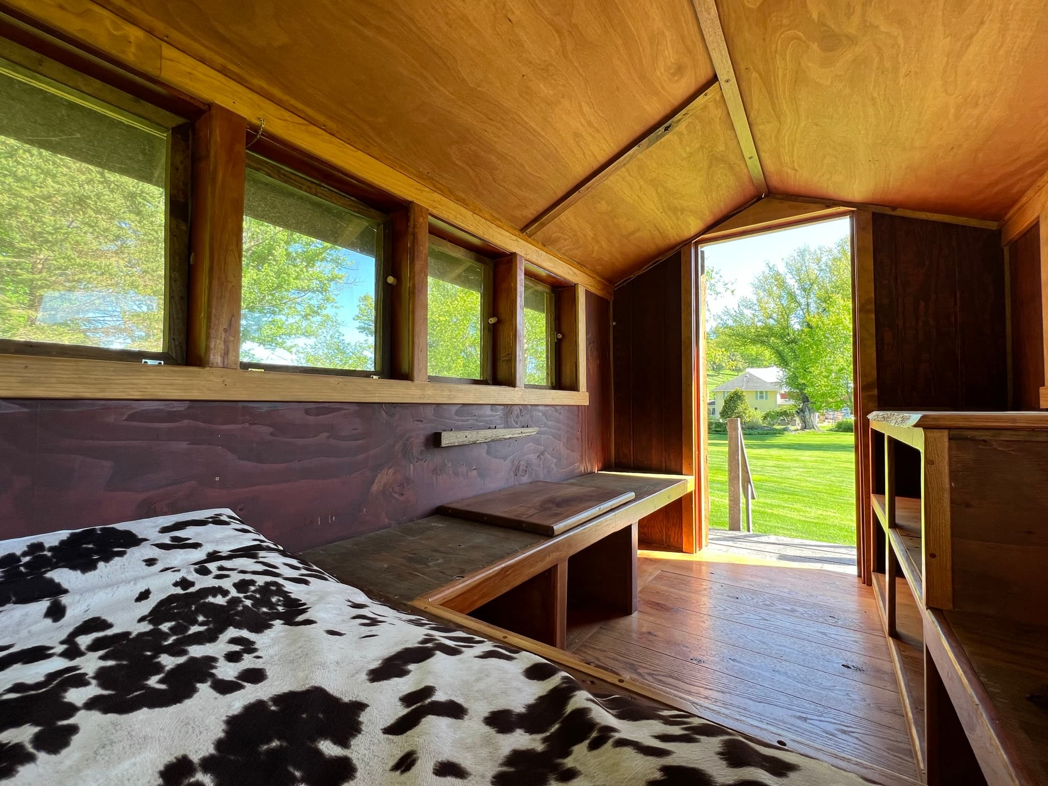 Interior to the left side of the Snuggalo from the bed area shows wooden bench seating under a bank of windows and the doorway leading to the stairs outside.