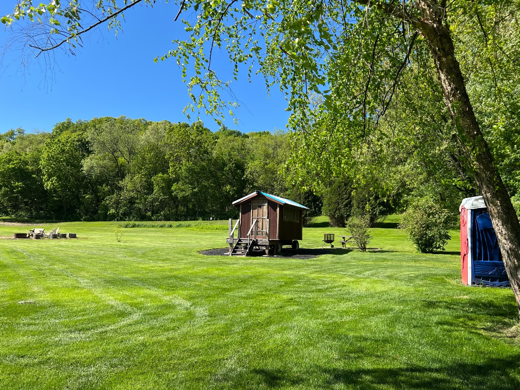 The Snuggalo is surrounded by green lawn at the edge of the woods.  There is a large firepit in the yard and a porta potty nearby next to the treeline.