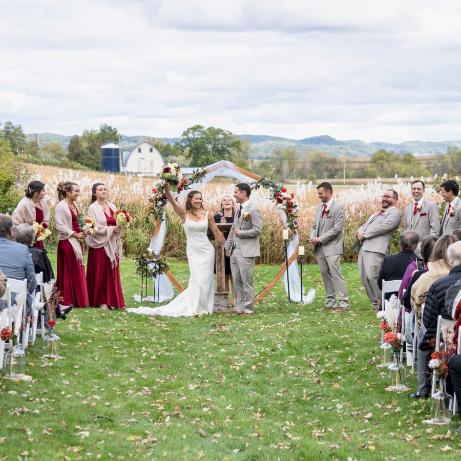 An outdoor wedding ceremony with the bride and groom rejoicing, and the wedding party and bystanders smiling and happy.