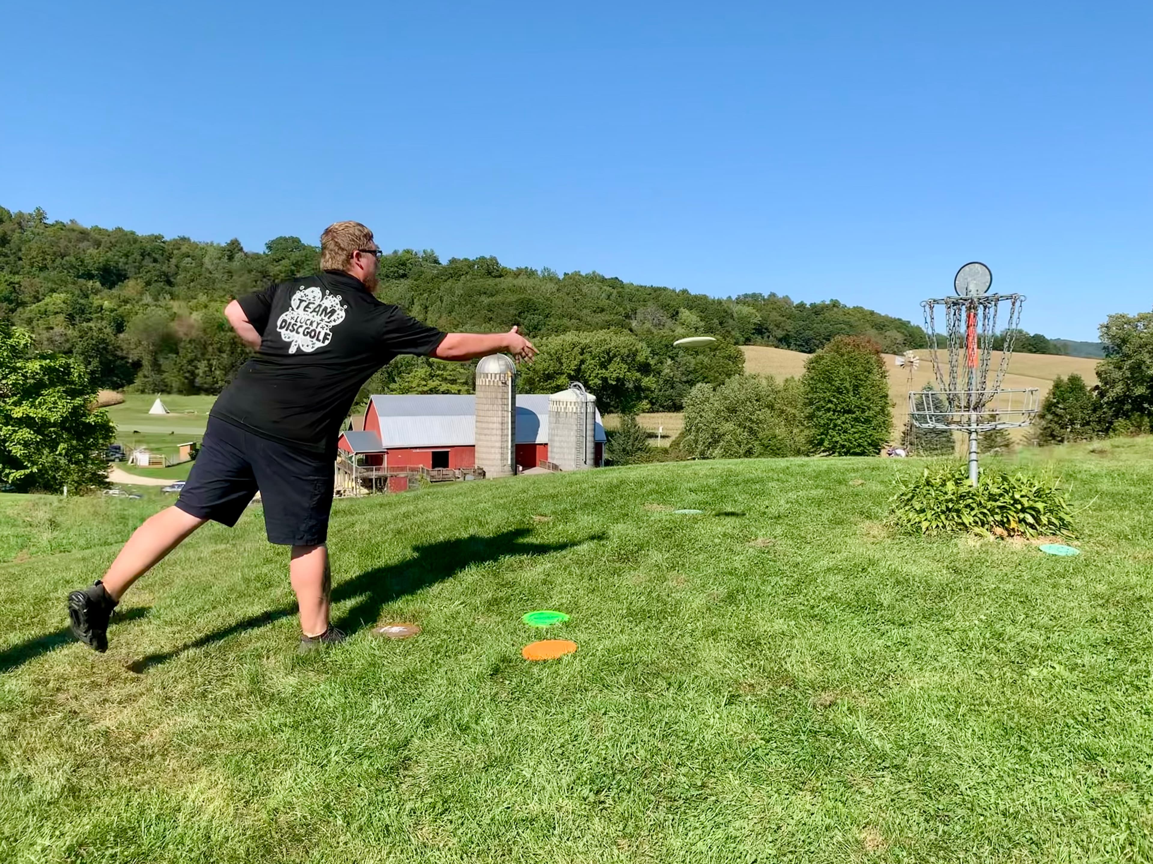 A man throwing a disc golf disc towards a disc golf basket