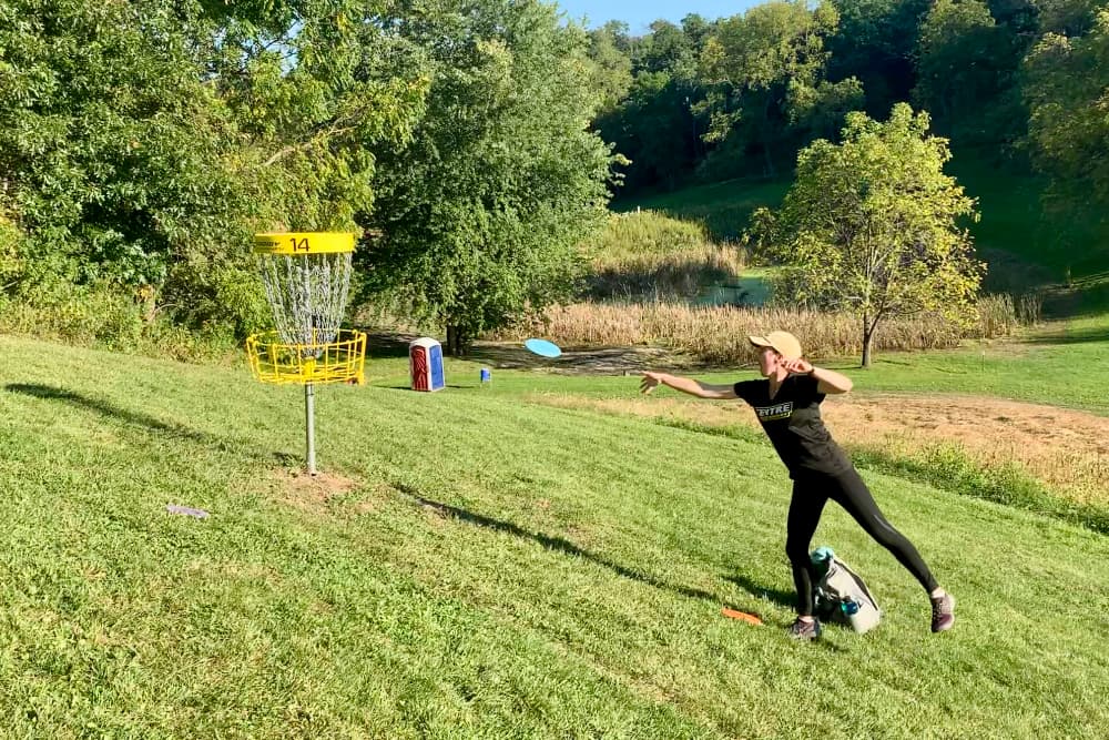 A woman throwing a disc golf disc towards a disc golf basket