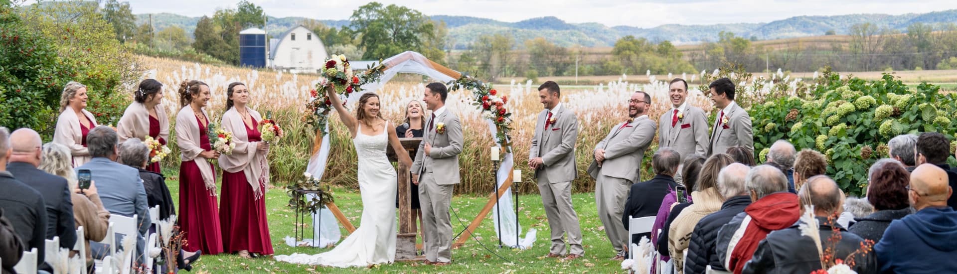 An outdoor wedding ceremony with the bride and groom rejoicing, and the wedding party and bystanders smiling and happy.