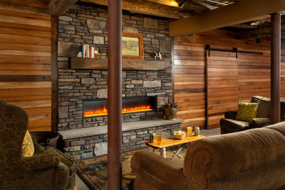 A large room with wood planks on the walls, wood beams, and a couch and chairs in front of a fireplace