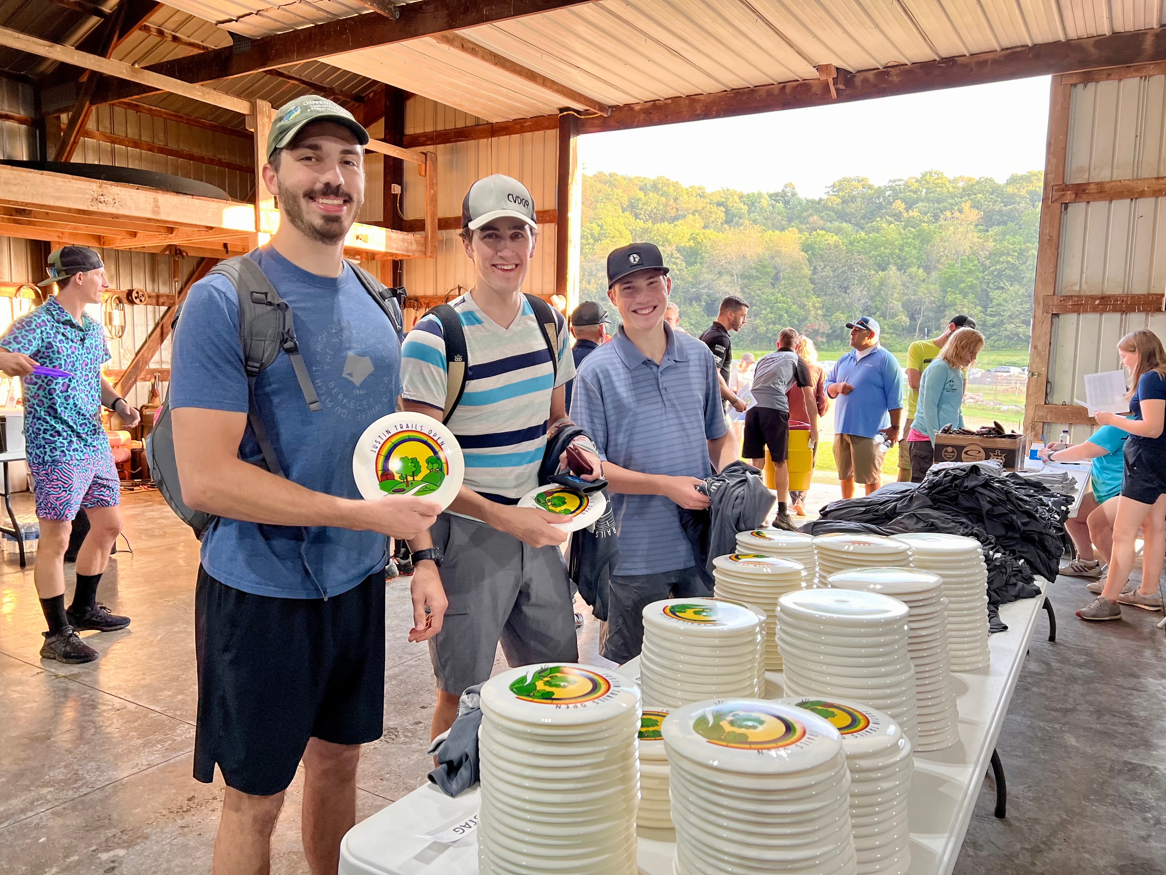 A group of people around a table with disc golf discs that say Justin Trails Open on them