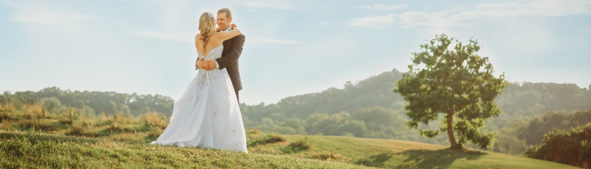 A couple in wedding attire embracing in the midst of rolling green hills and trees