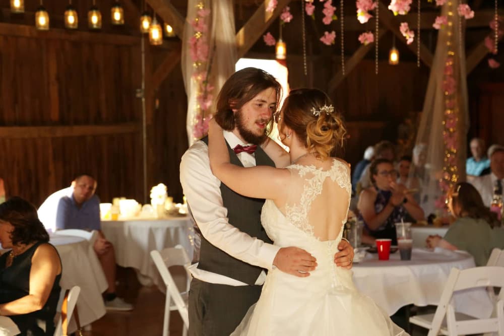 A bride and groom sharing an intimate dance inside an elegant barn with guests looking on.