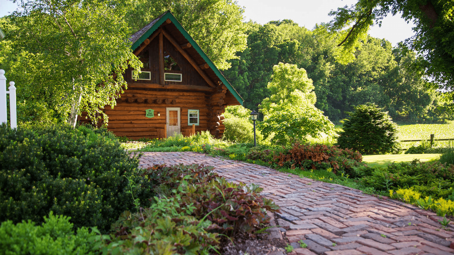 log cabin with green roof and red brick pathway set in greenery and trees