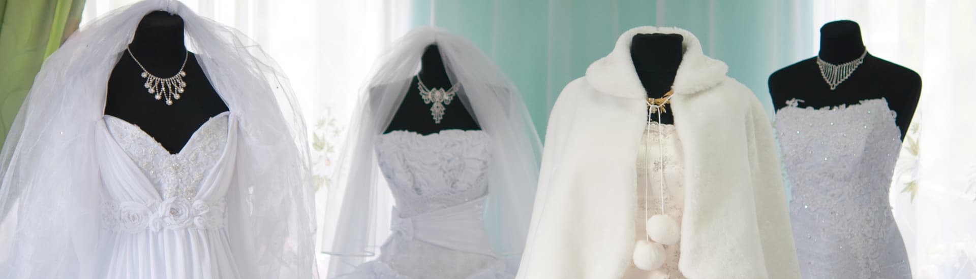 Four elegant white wedding dressing on black forms with sparkling necklaces, and veils