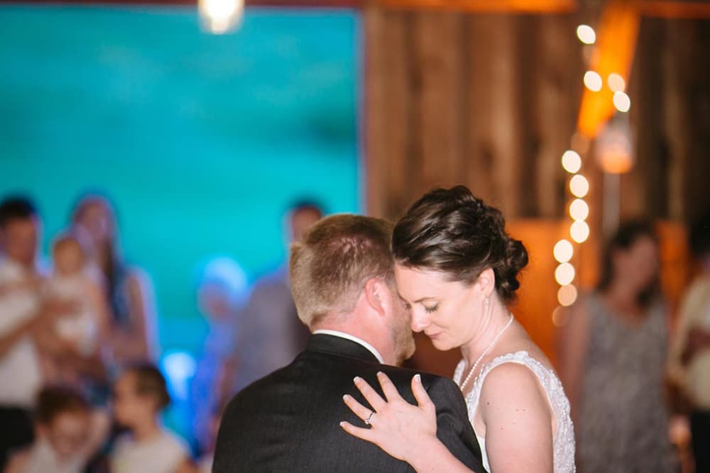 A wedding couple dancing in an indoor barn with onlookers watching them.