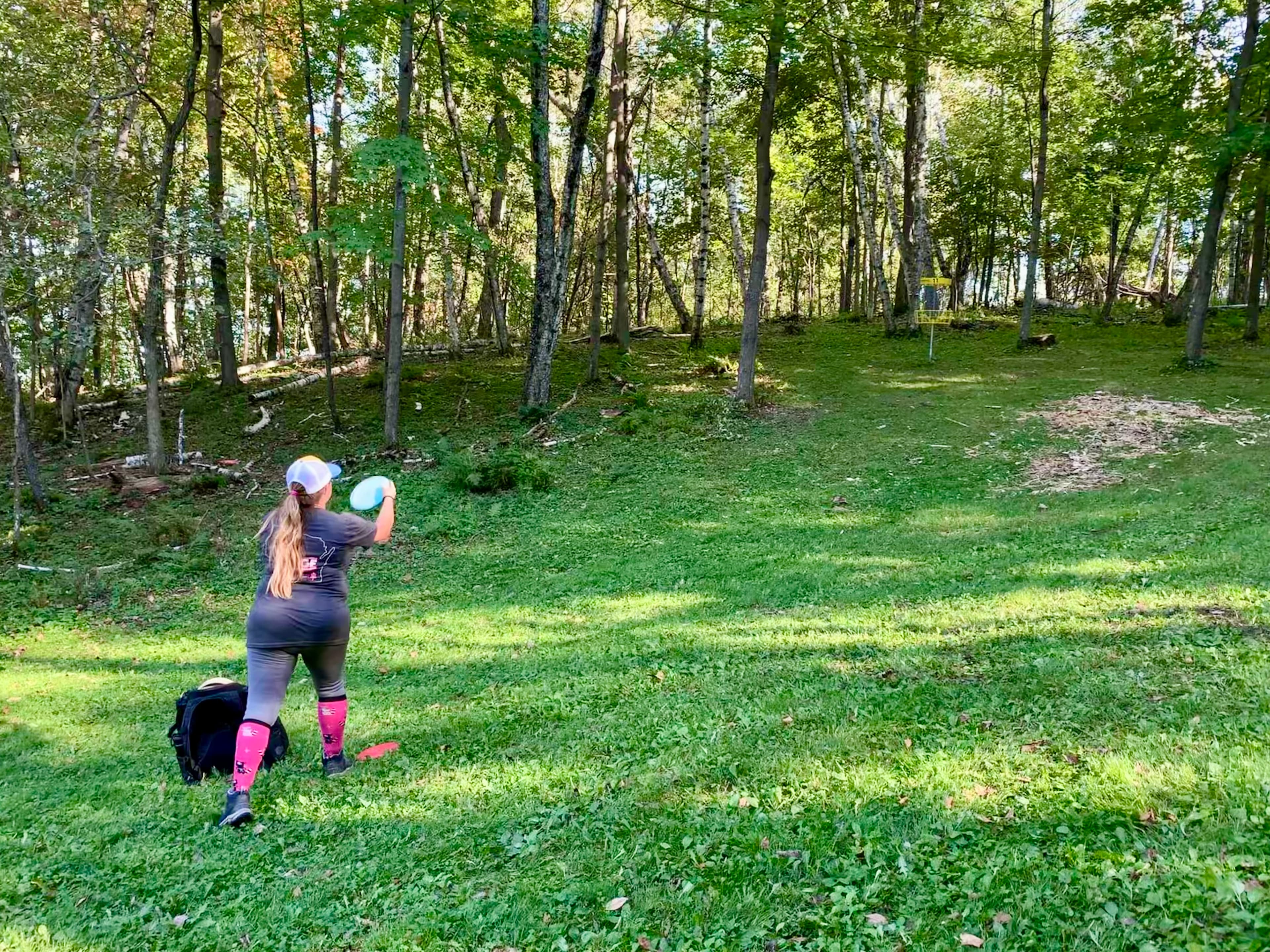 A woman throwing a disc golf disc towards a disc golf basket