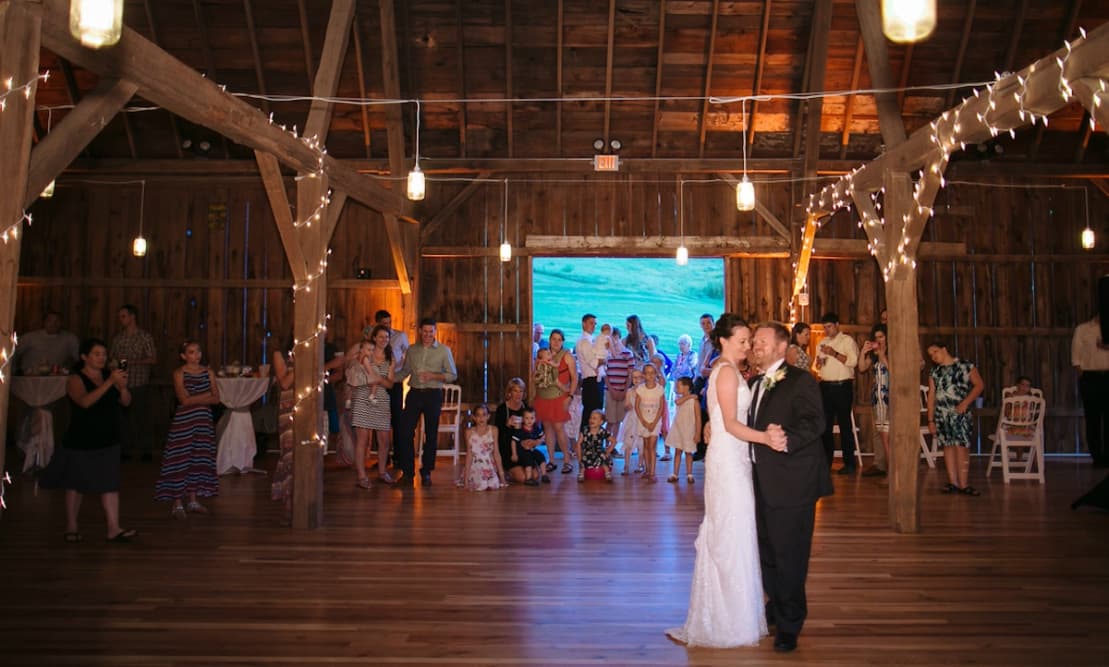 A bride and groom sharing a dance in a large elegant barn with people watching them.