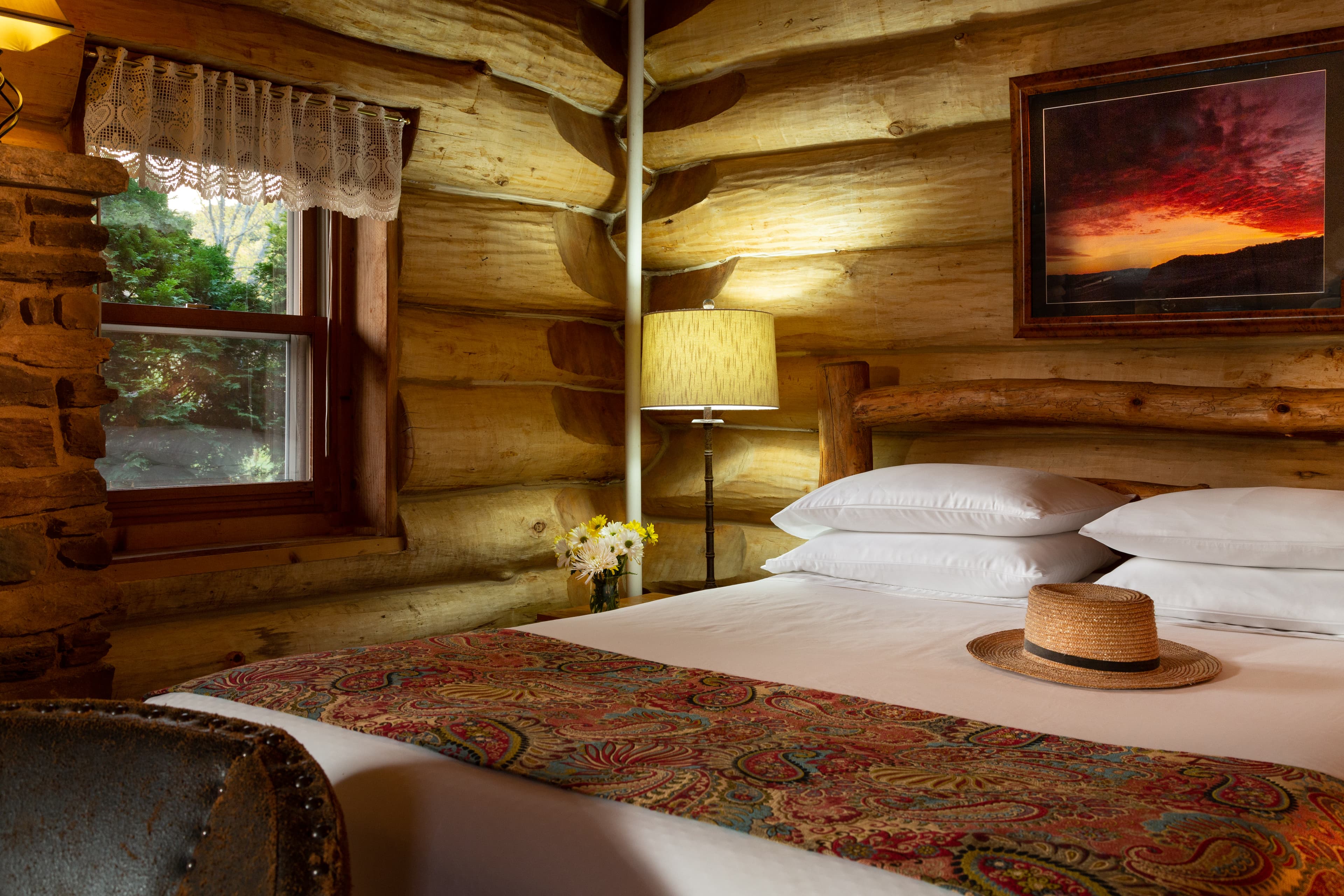Inviting queen bed on first floor next to fireplace and natural wood log walls.