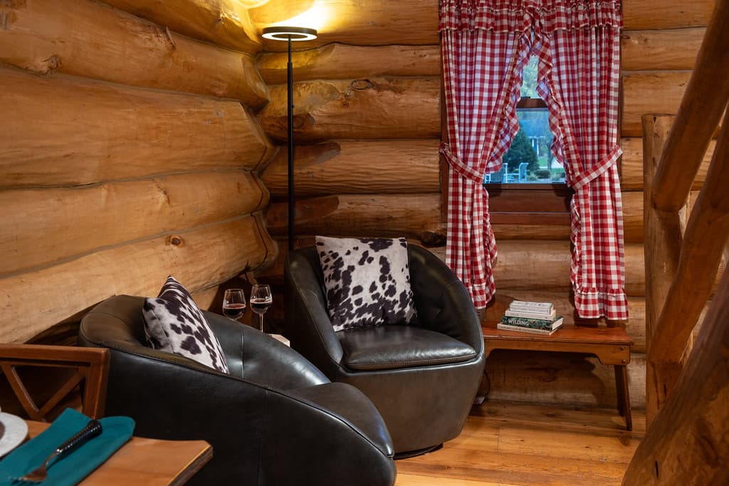 A sitting area in a log home with 2 leather armchairs with glasses of red wine and books on nearby tables