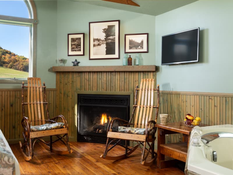 Bent wood rocking chairs in front of corner fireplace, HH Bennett photos hanging on the wall with flat screen TV beside, and edge of whirlpool tub just visible to the side.