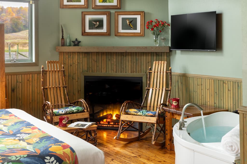 Bent wood rocking chairs in front of corner fireplace, HH Bennett photos hanging on the wall with flat screen TV beside, and edge of whirlpool tub just visible to the side.