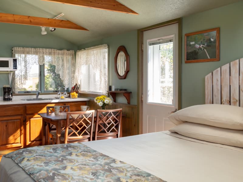Kitchenette with table and chairs in background and king bed with white washed fence style headboard in foreground.