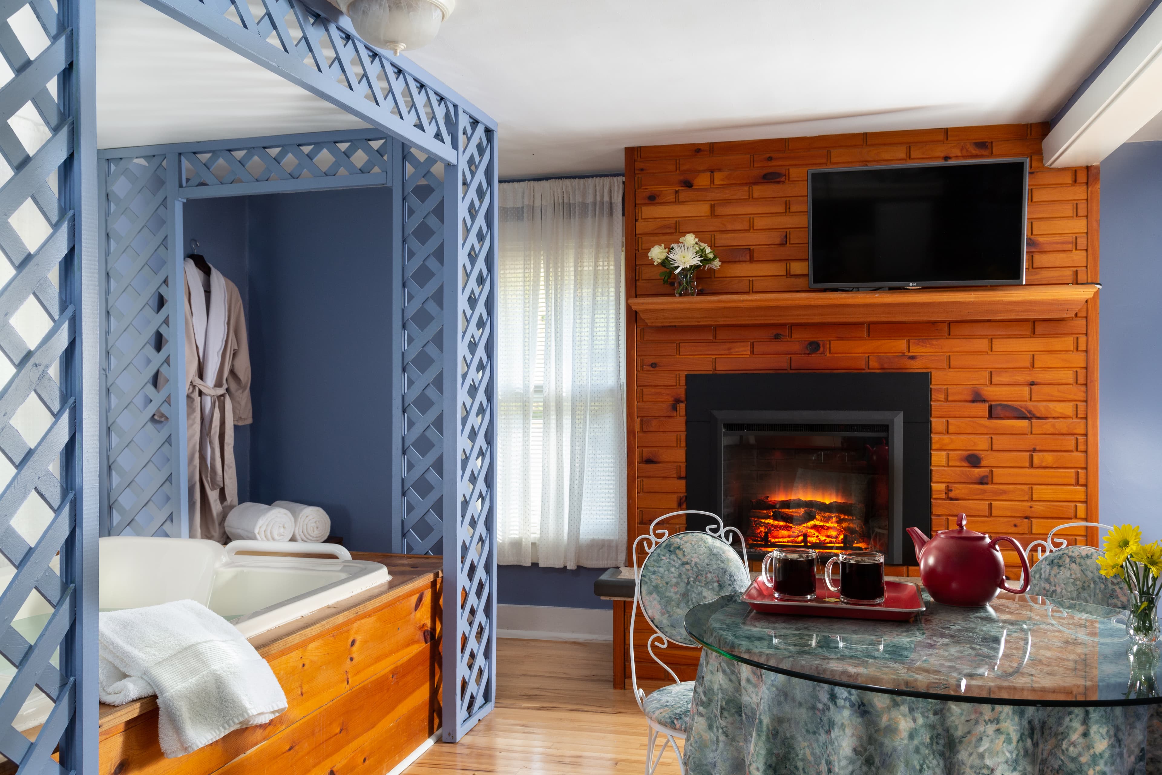 Charming suite with lovely periwinkle blue walls, electric fireplace with pine brick surround, round glass top table with chairs for two, and a large whirlpool tub.