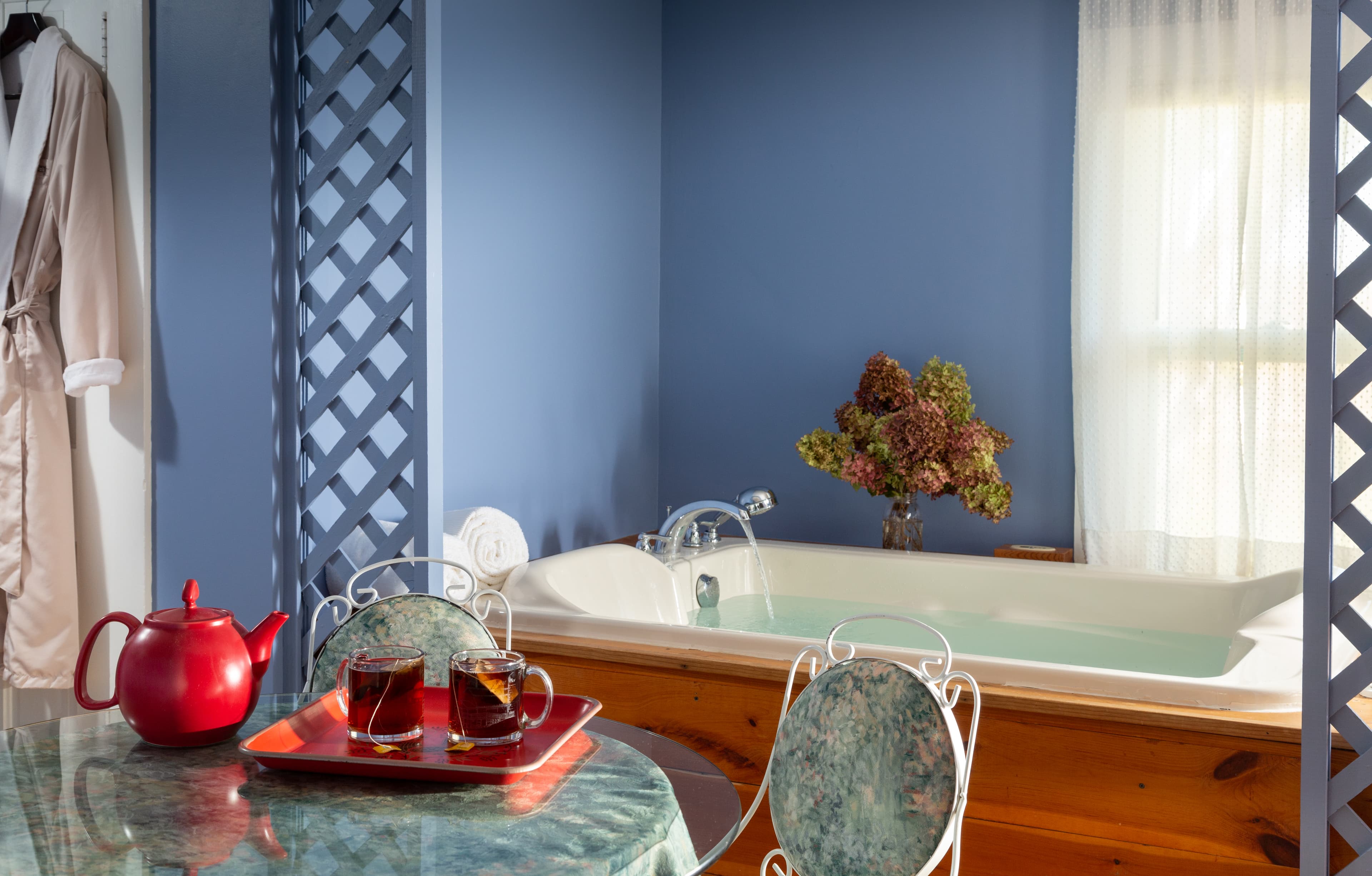 Sweet dining set in the foreground with tea service for two and in the background is a very large BainUltra whirlpool bathtub with natural wood surround.