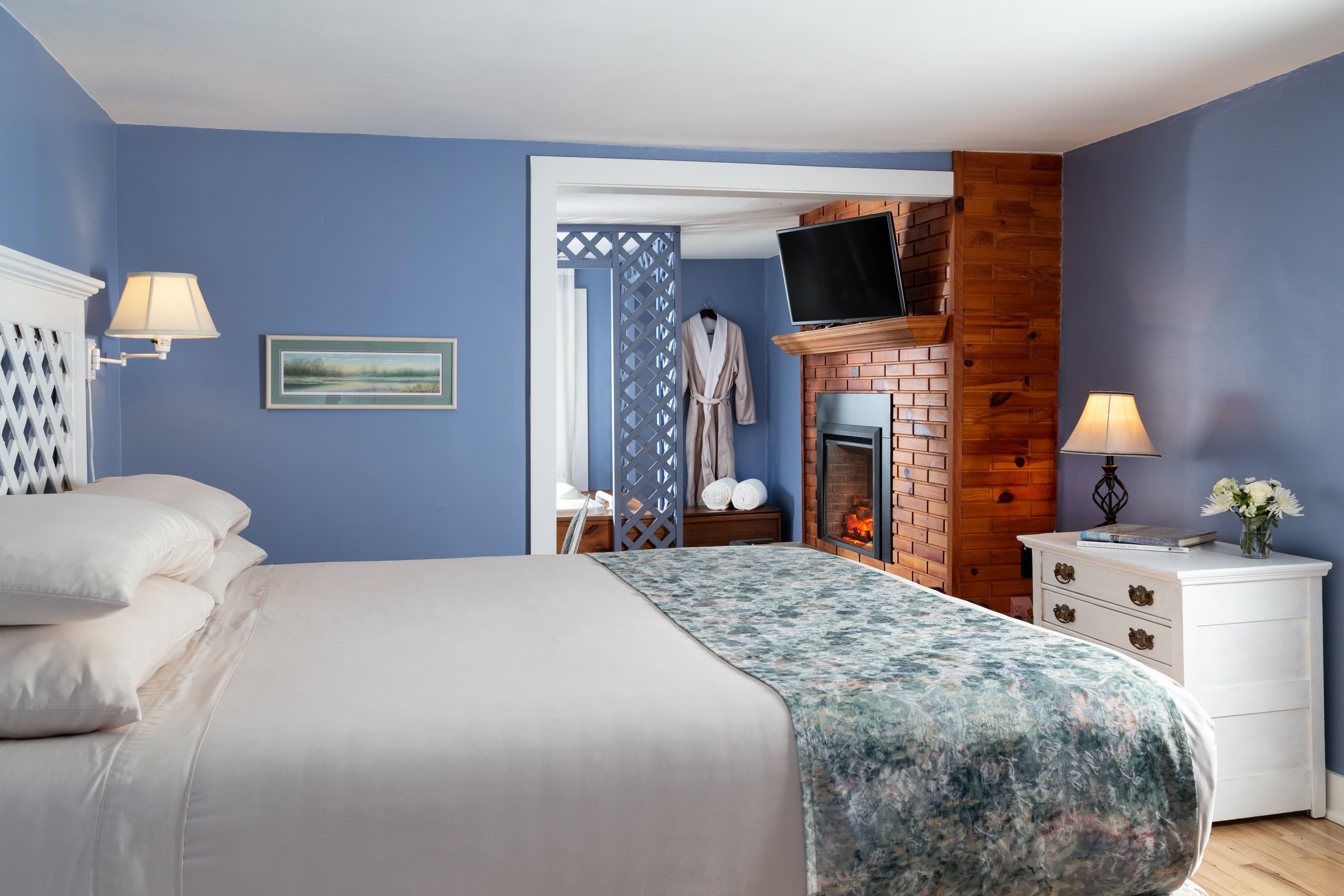 Lattice surrounding BainUltra whirlpool bathtub, pine wood brick surrounding electric fireplace, and king bed with white lattice headboard in the foreground.
