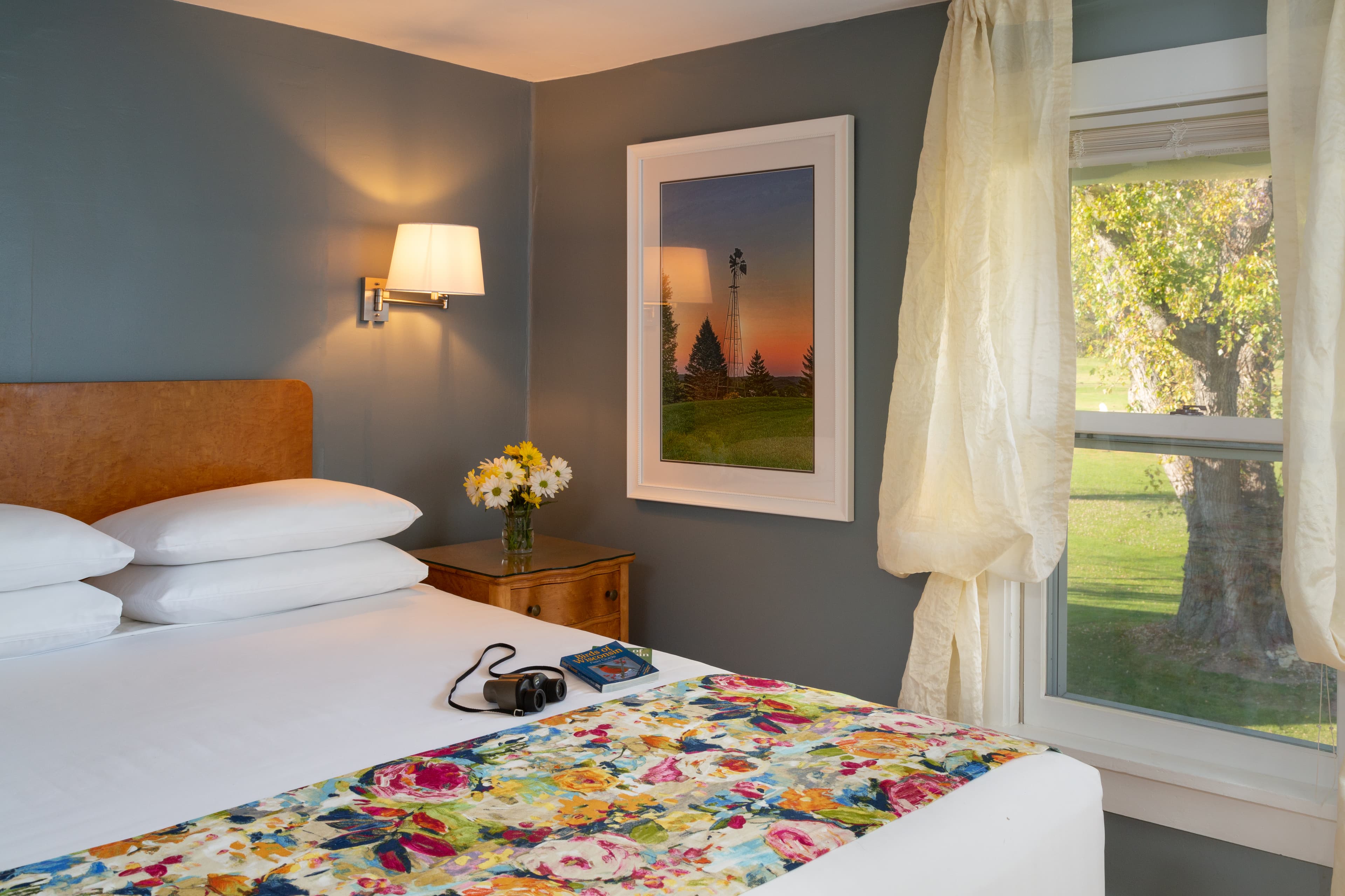 Queen size bed with white sheets and a floral bedspread and window with view of 150 year old Silver Maple tree