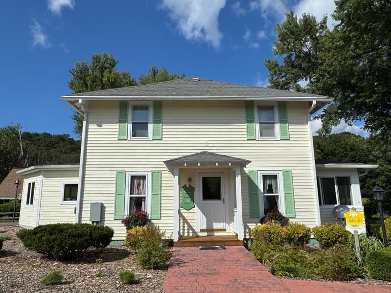 1920 yellow Foursquare Farmhouse with green shutters and a 150 year old Silver maple tree and Eastern White pine tree in the front yard.