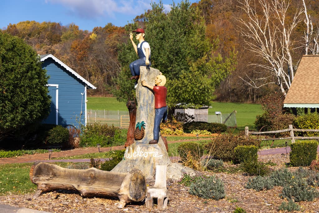 A partially cut down wood tree with 2 carved figurines on the tree and a wood bench next to the tree