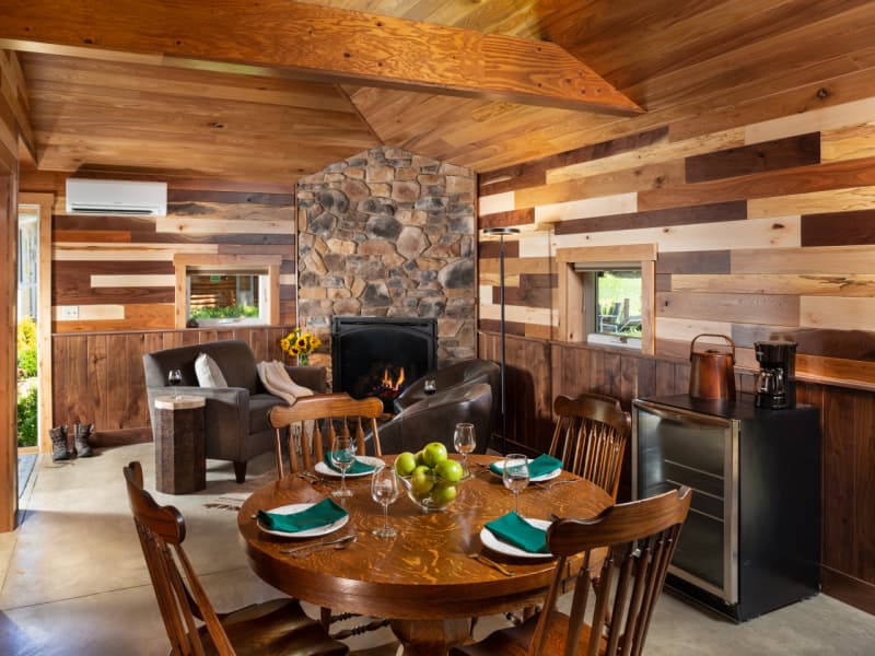 Round wooden table and chairs set for 4 in foreground and cozy seating area near corner fireplace inside Sunrise Cottage.