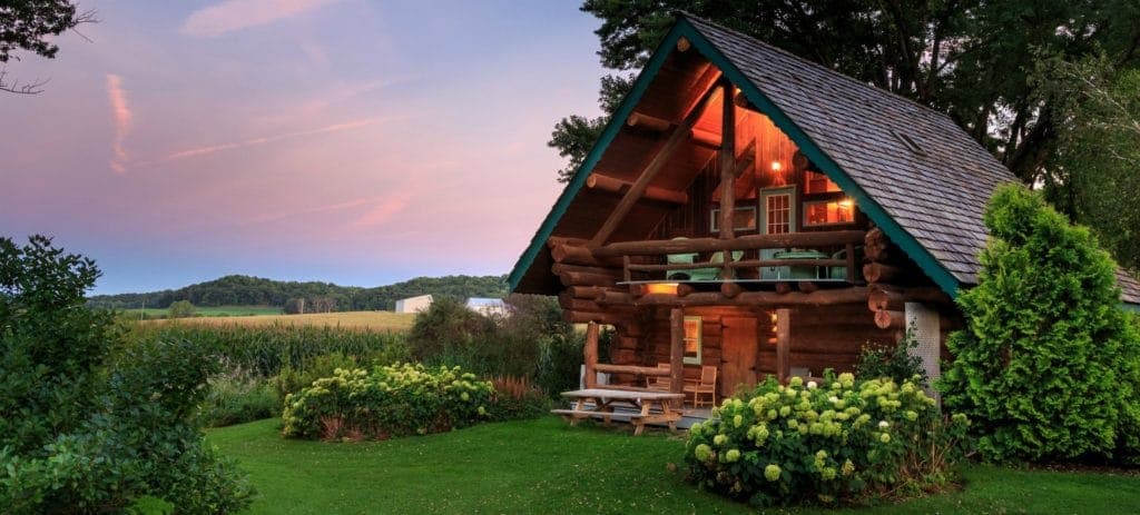 A cozy log cabin surrounded by greenery and a sunset sky.