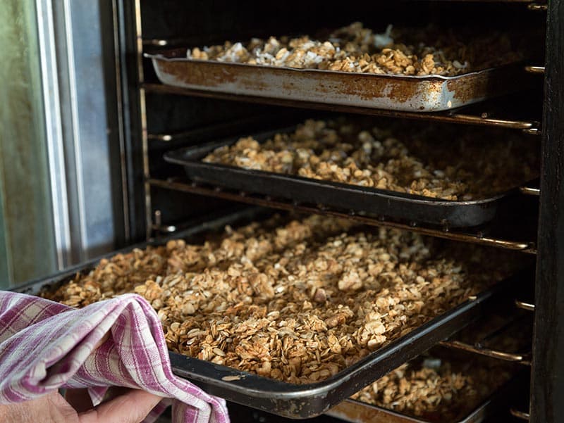 Several trays of freshly baked granola being pulled from the oven