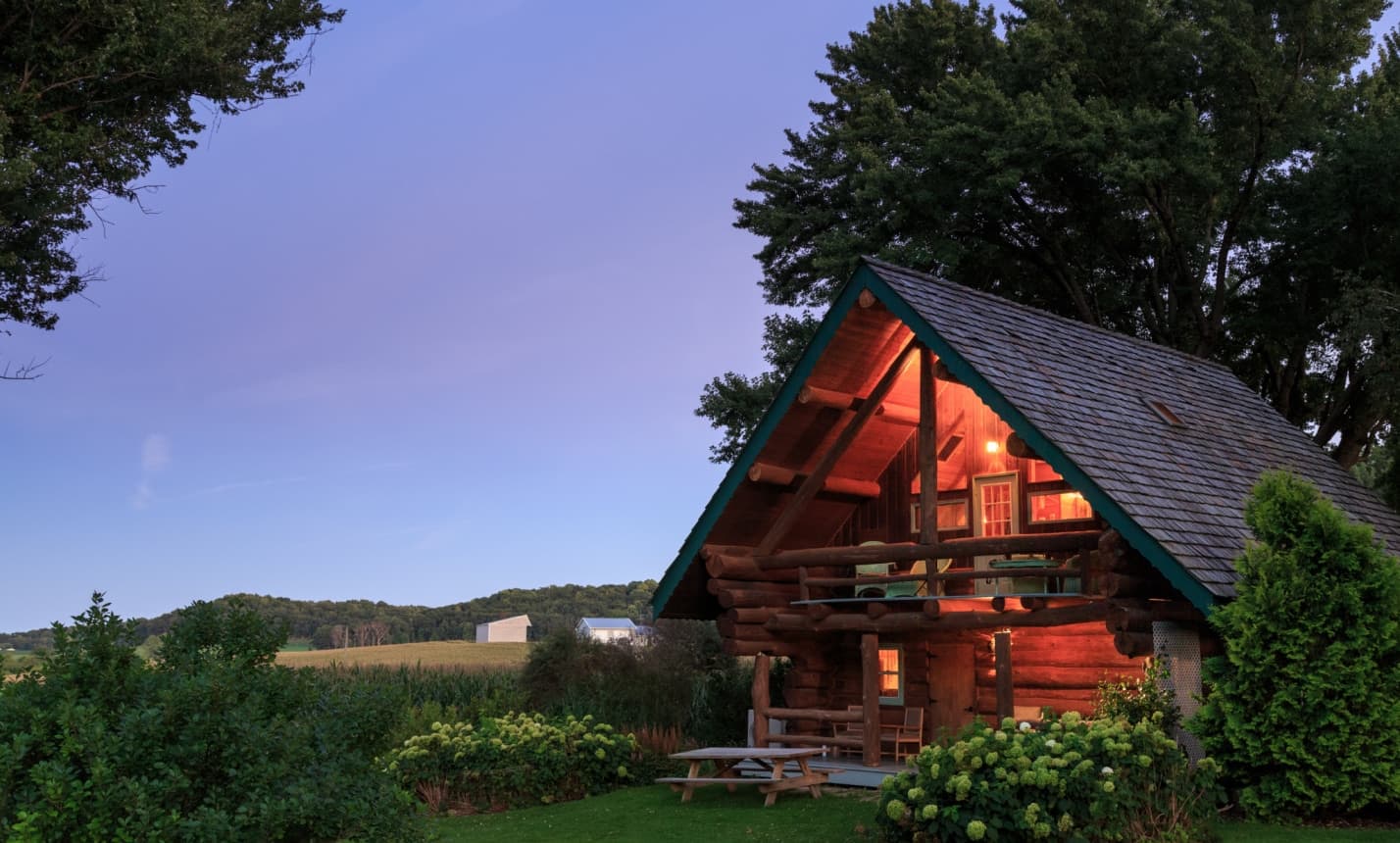 A cozy log cabin surrounded by greenery under a twilight sky.