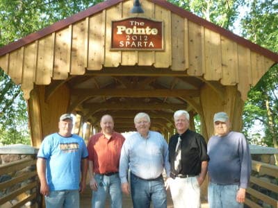 Five men stand together under a wooden bridge with a sign that reads "The Pointe 2012 Sparta."