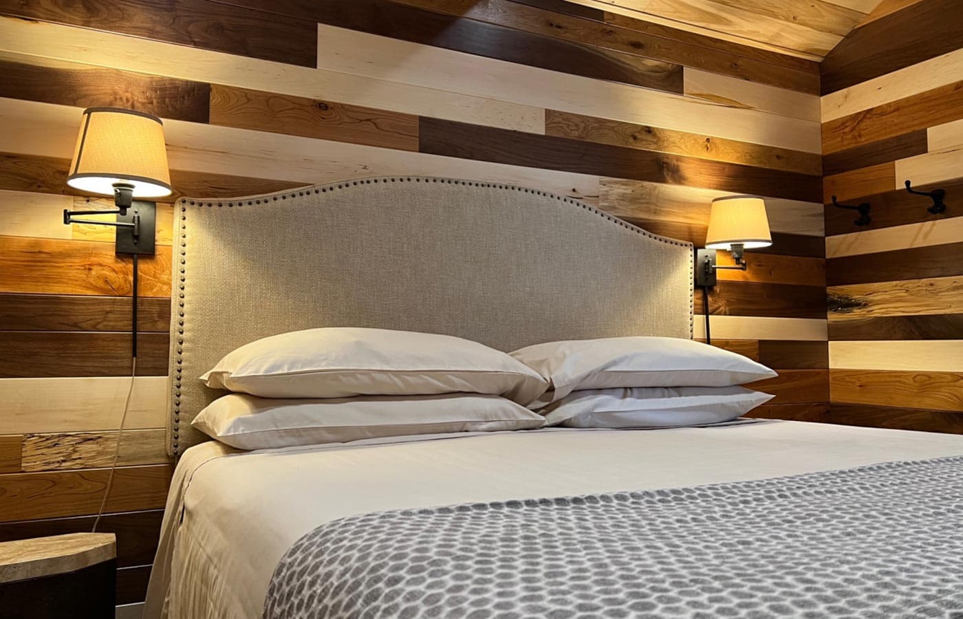 A cozy bedroom with a neatly made bed, soft pillows, and wooden accent walls.