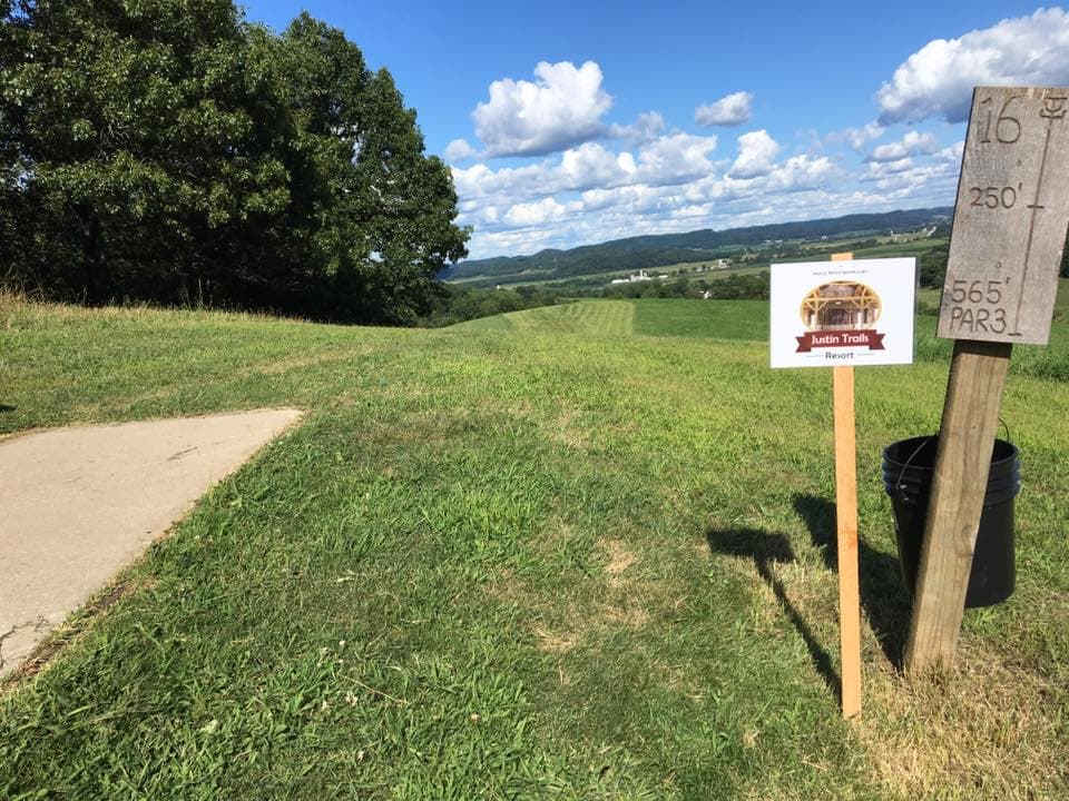 A scenic view of a golf hole sign indicating the distance and par, with green fields and a blue sky in the background.