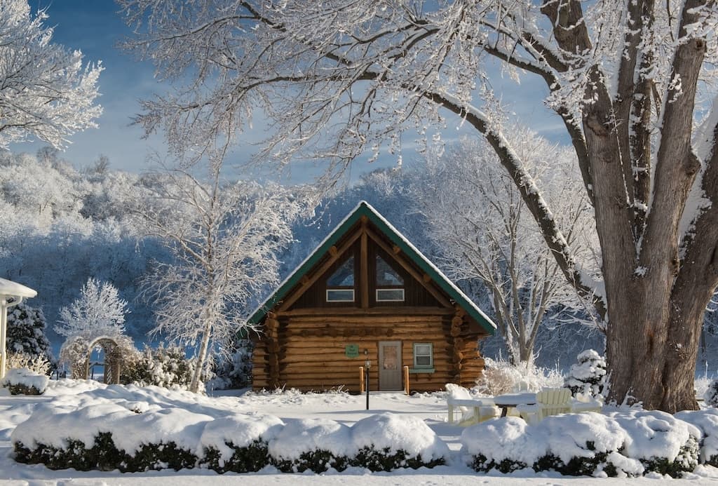 A cozy log cabin surrounded by snow-covered trees and a winter landscape.