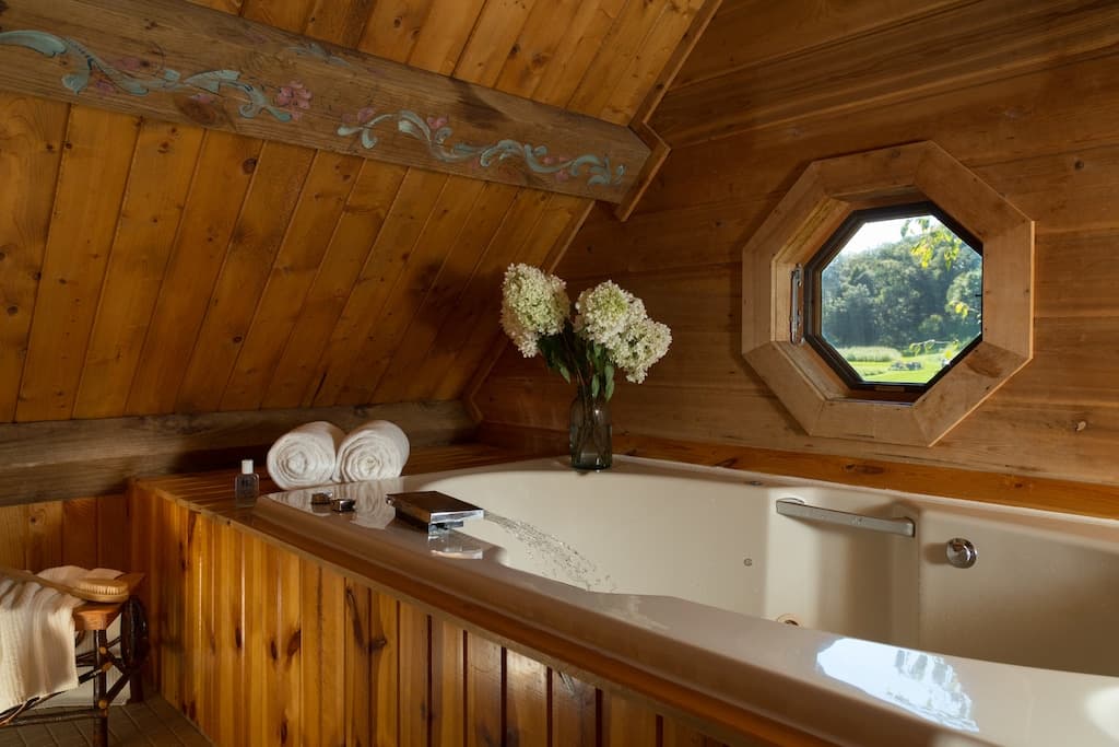 Cozy wooden attic bathroom with a whirlpool tub and a window overlooking nature.