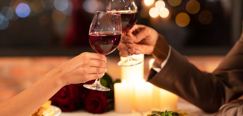 Two glasses of red wine being clinked together in a romantic dining setting.