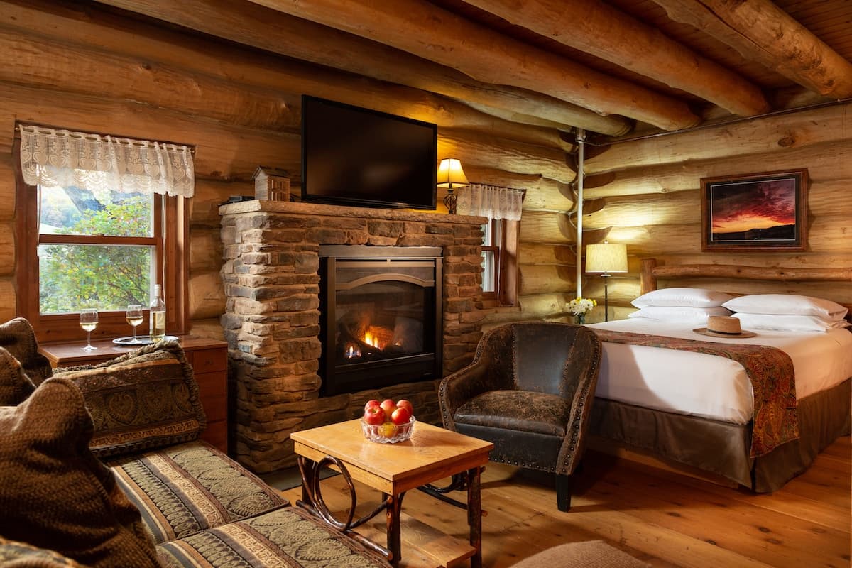 Cozy log cabin interior featuring a stone fireplace, a comfortable seating area, and a queen-sized bed.