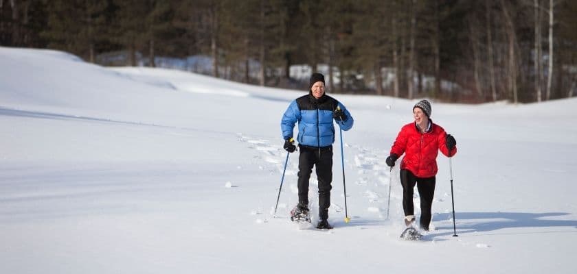 A man and a woman are snowshoeing together on a snowy landscape.
