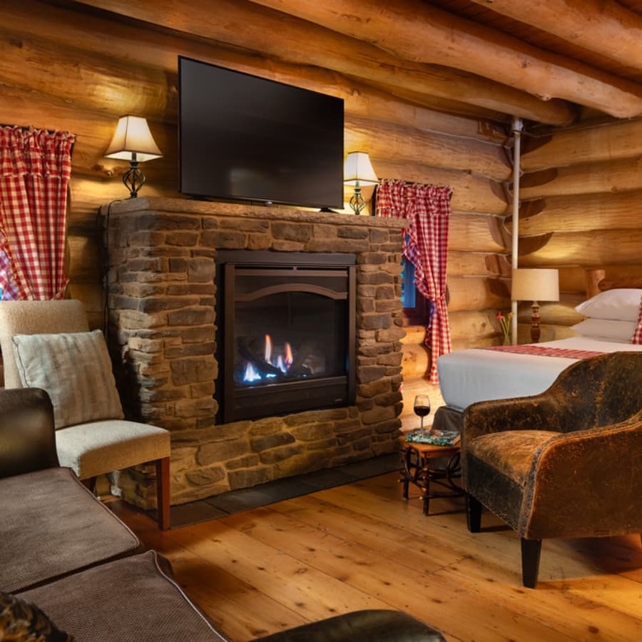 Cozy log cabin interior with a stone fireplace, TV, and comfortable seating.