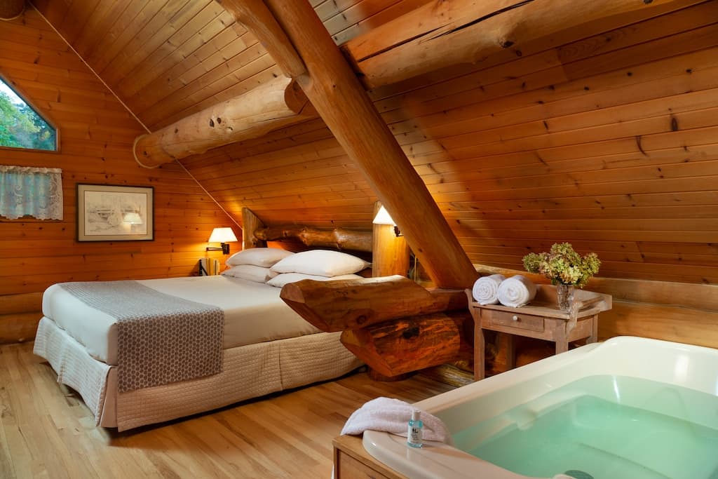 Cozy wooden attic bedroom with a large bed, a jacuzzi, and rustic decor.