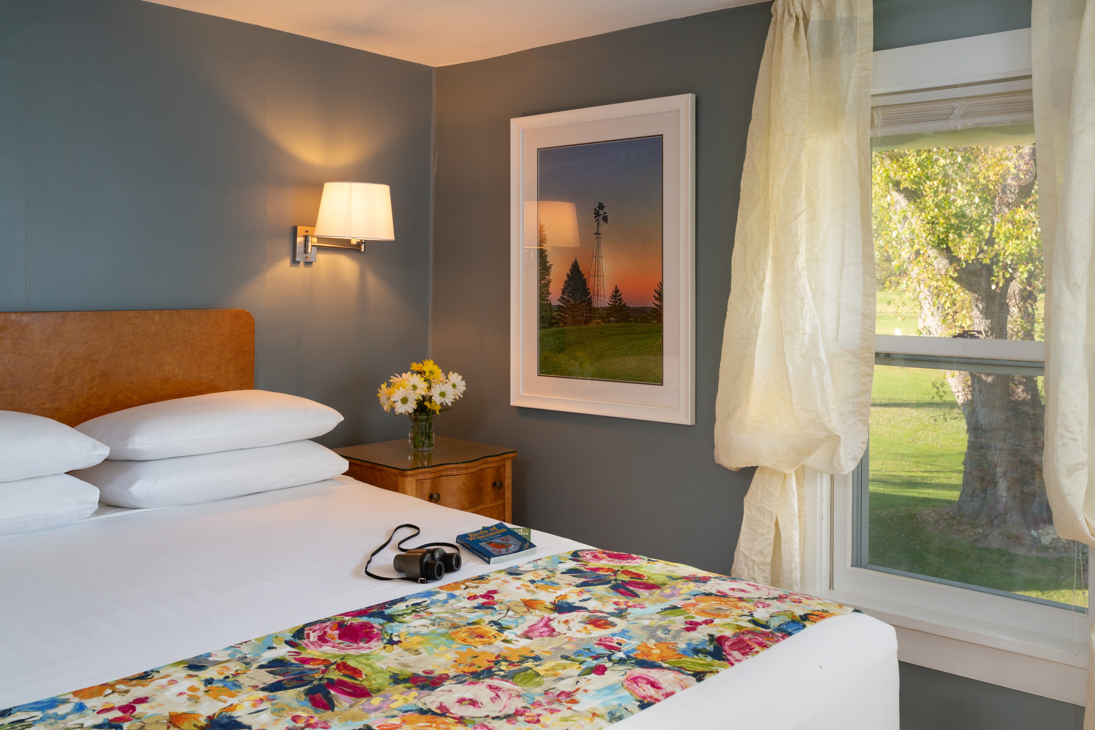 Queen size bed with white sheets and a floral bedspread and window with view of 150 year old Silver Maple tree
