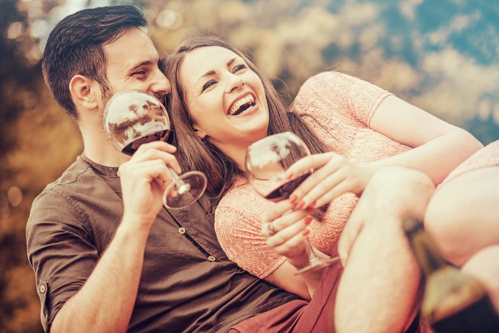 A couple joyfully sharing a moment with glasses of red wine outdoors.