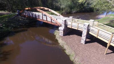 A wooden arched bridge spans a calm river, surrounded by greenery.