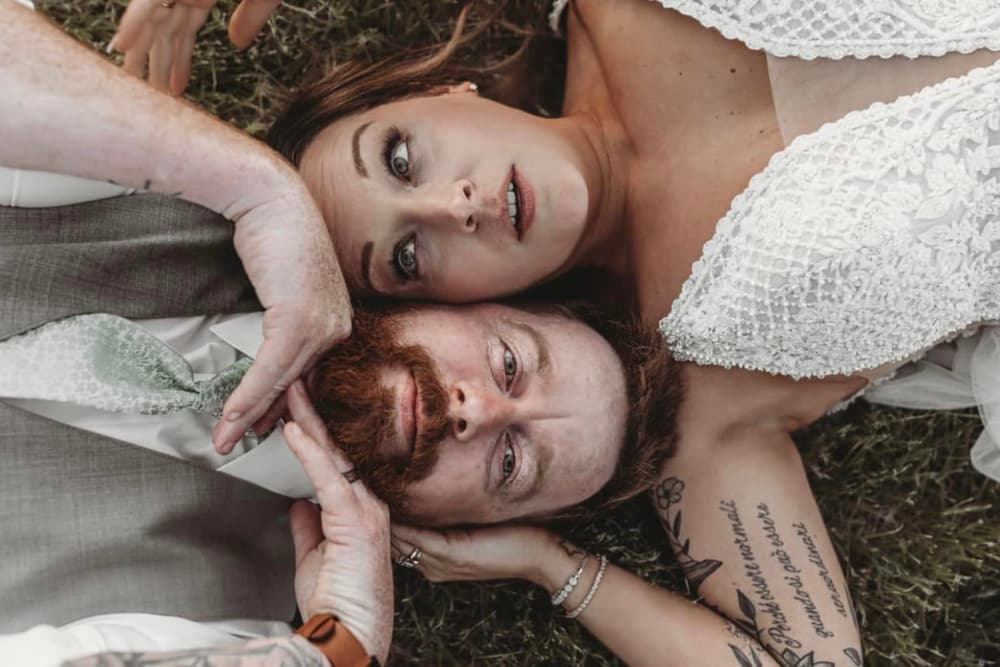 A couple dressed in wedding attire on the ground with their heads next to each other
