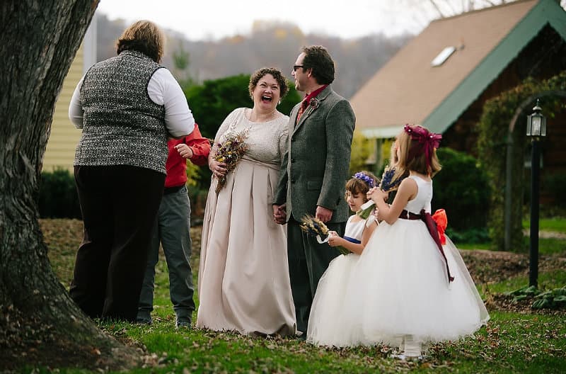 A joyful couple stands hand in hand surrounded by friends and children at an outdoor wedding celebration.